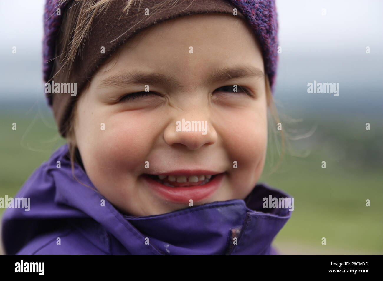Young girl in purple hiking jacket with cheeky grin winking Stock Photo