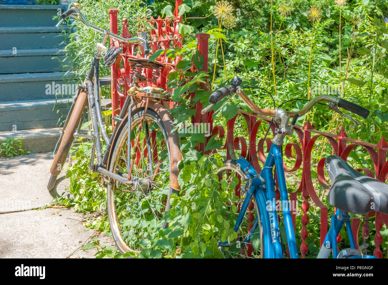 Two vintage bicycles propped against a bright red wrought iron fence in the Kensington Market District of Toronto. Stock Photo