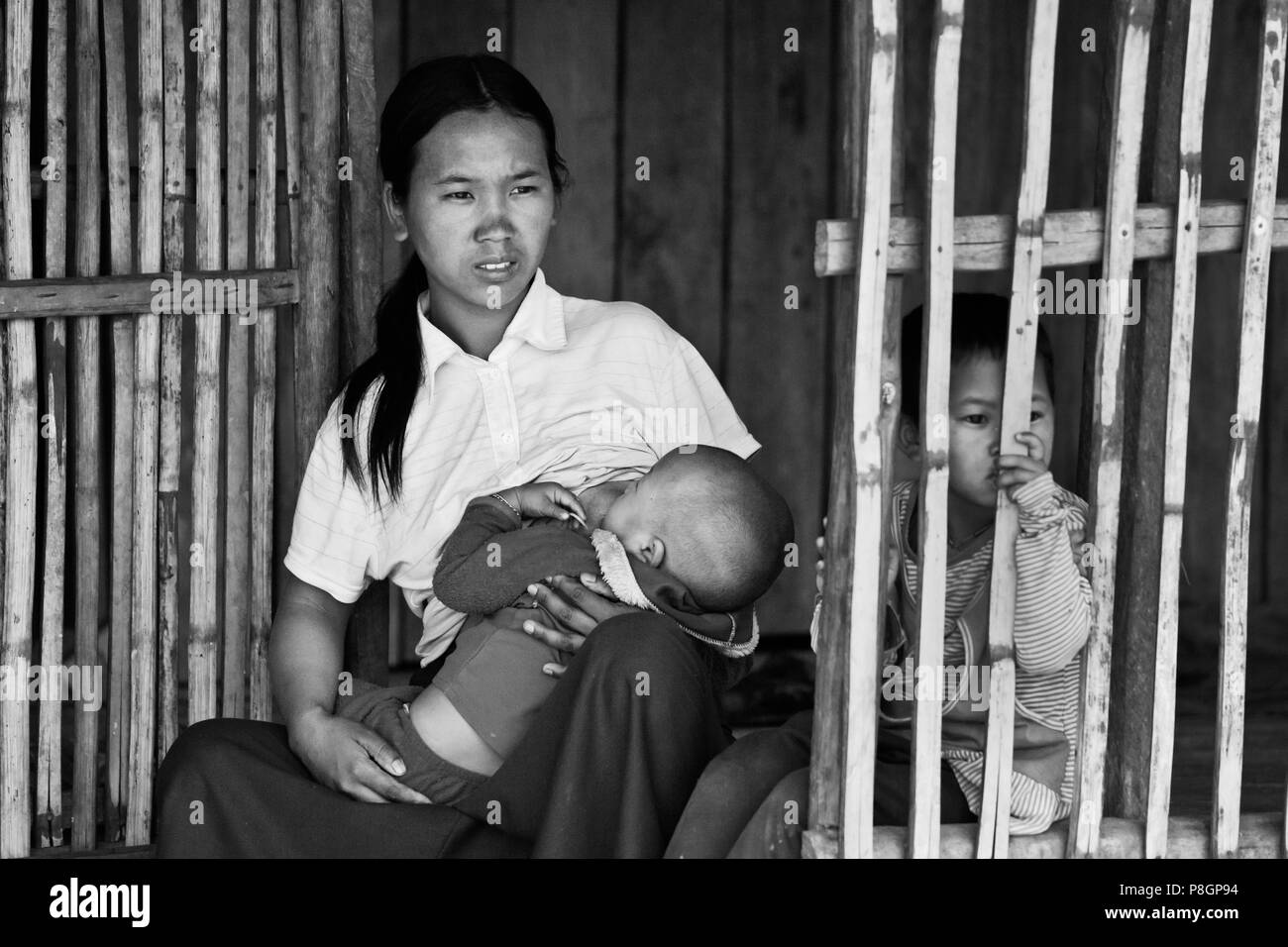 A woman of the AKHA tribe nurses a child in her bamboo house -  village near KENGTUNG or KYAINGTONG - MYANMAR Stock Photo