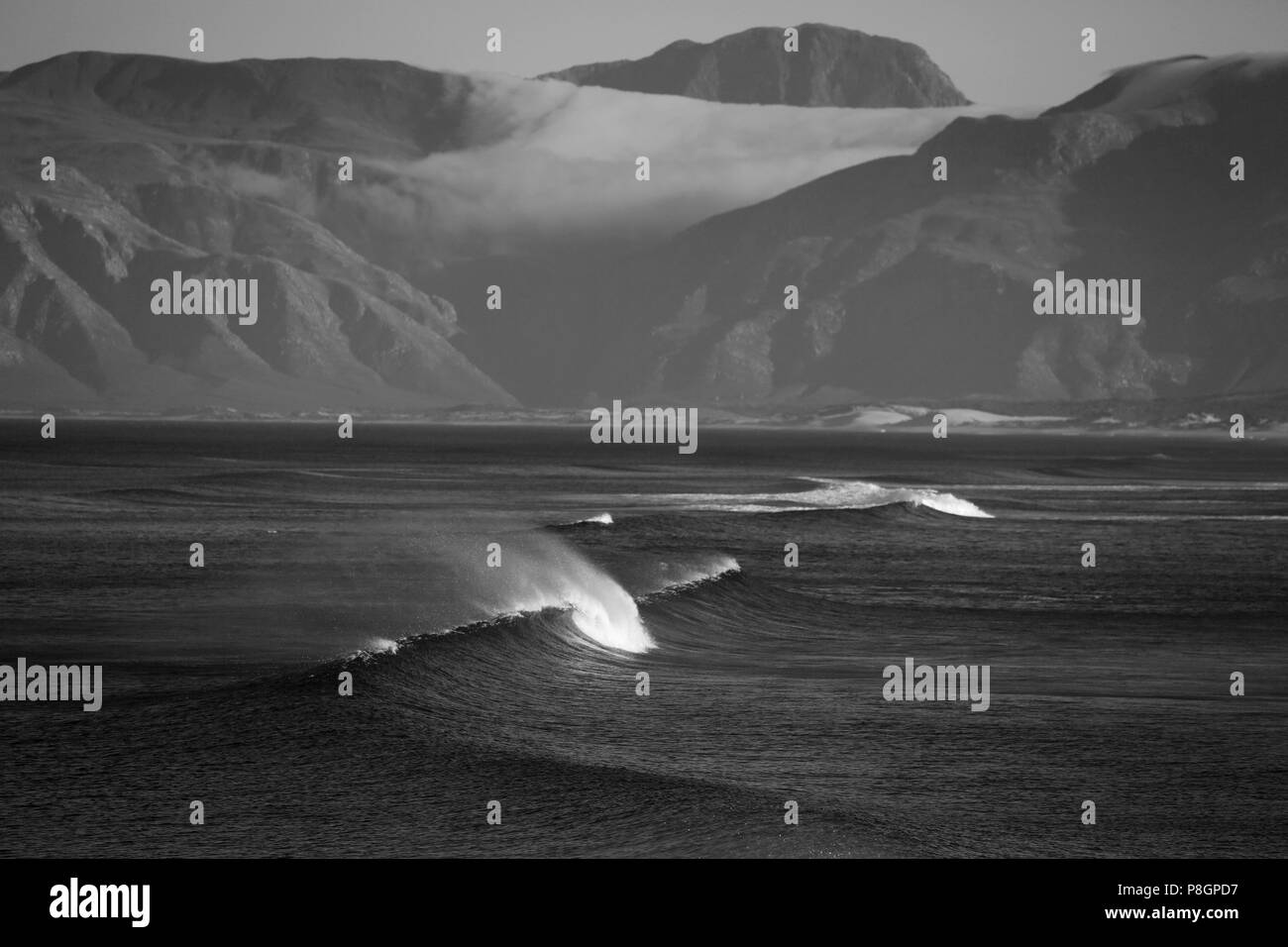 Black and white landscape of a breaking wave with big mountains in the background in South Africa Stock Photo