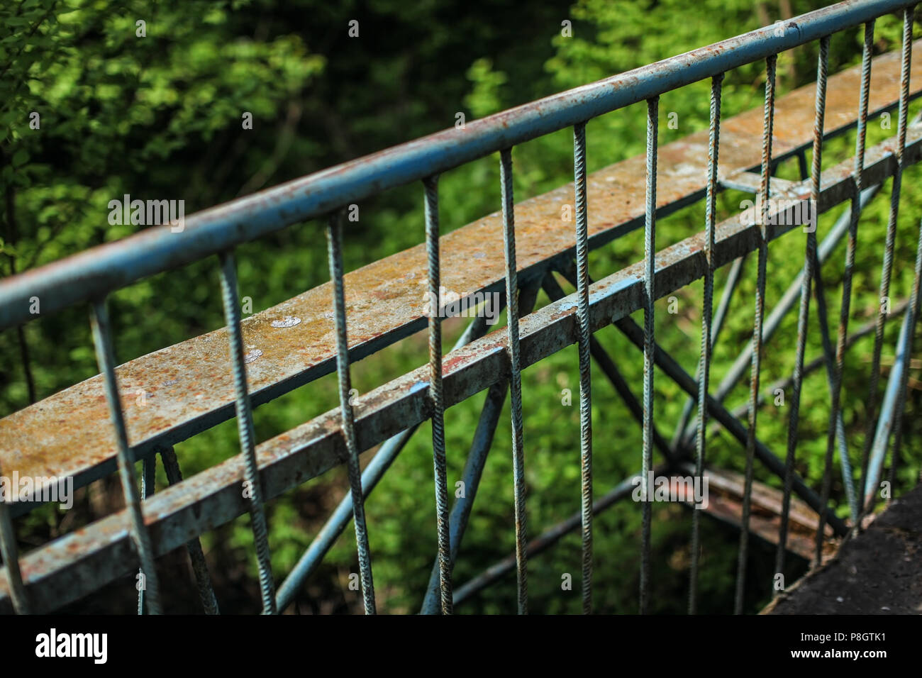 Old metal guard rail of bridge, with blurred green forest in background. Stock Photo