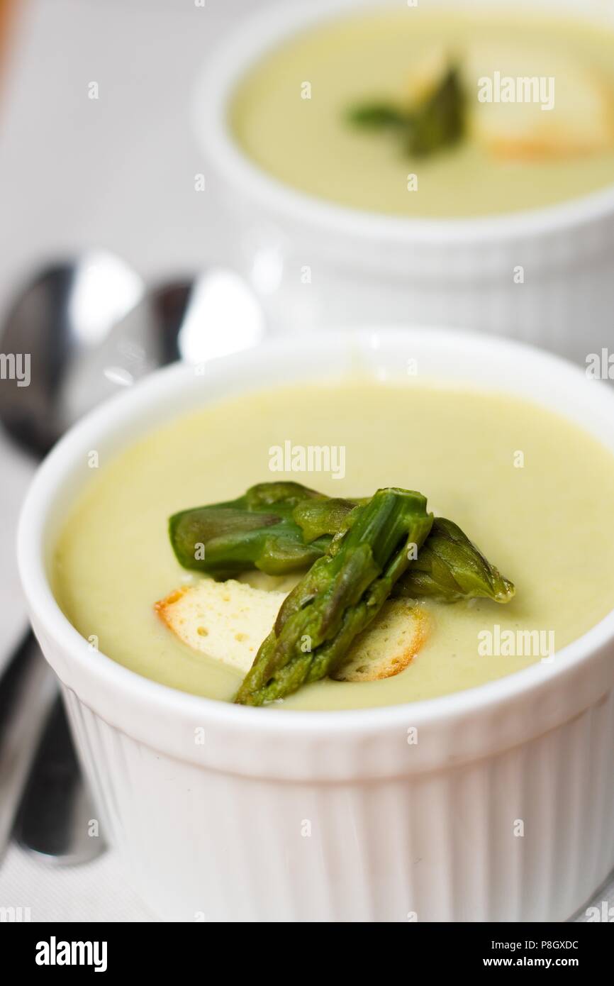 Healthy summer meal. Asparagus soup with creamy texture served in white cups with bread chip and green asparagus Stock Photo