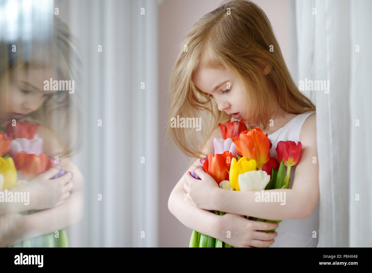 Adorable smiling little girl with tulips by the window Stock Photo