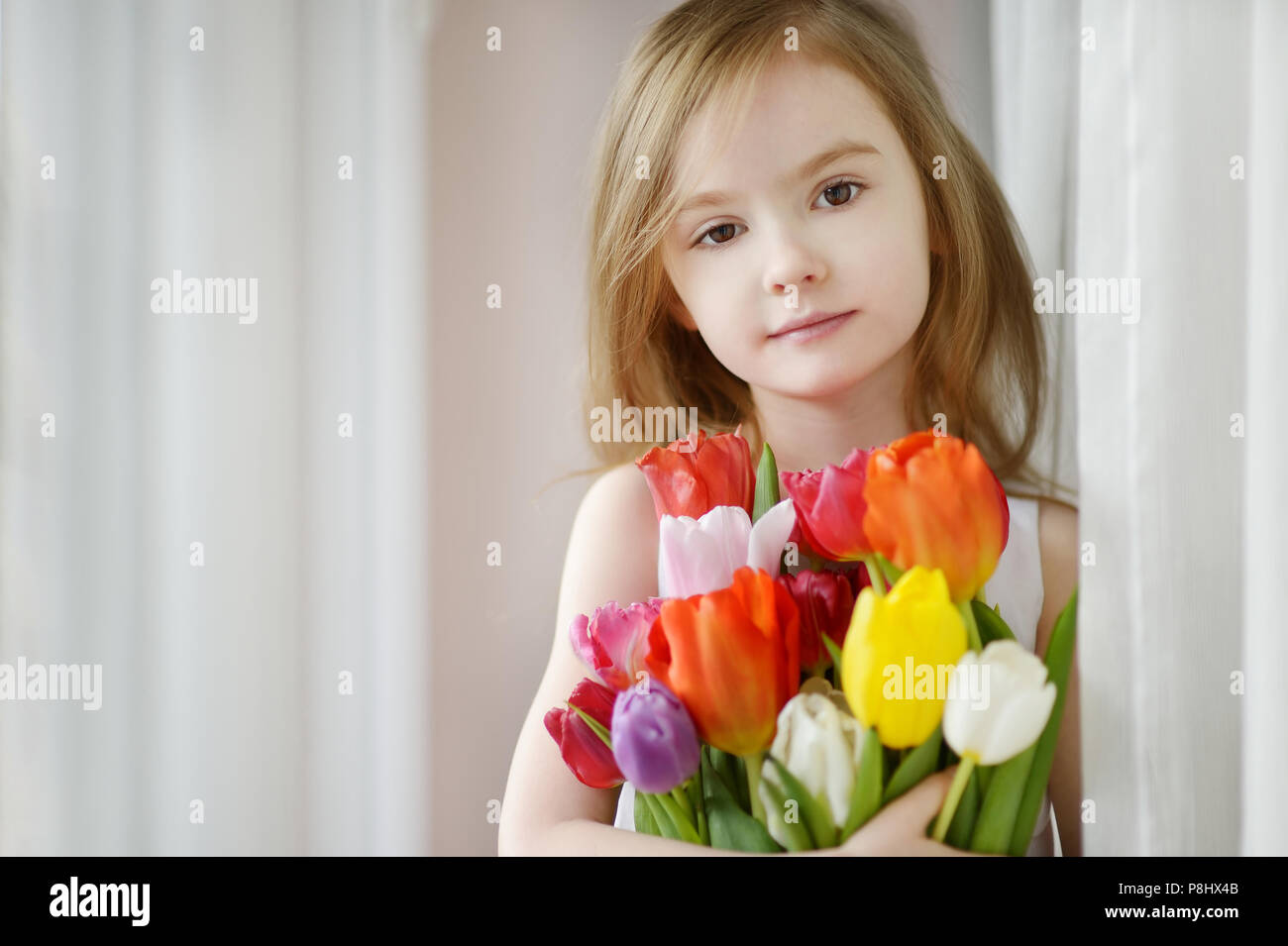 Adorable smiling little girl with tulips by the window Stock Photo