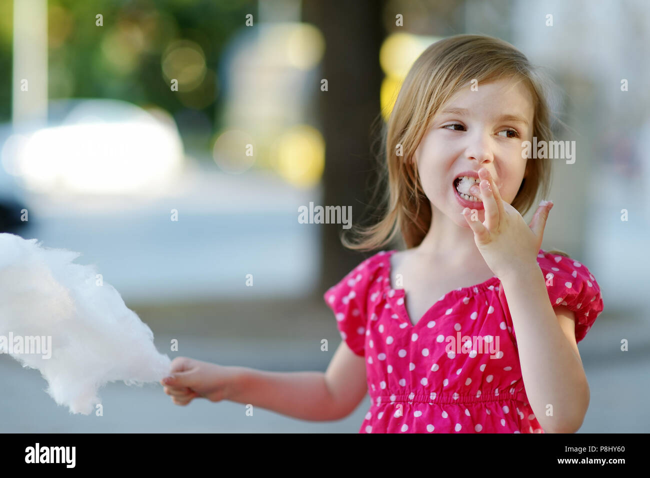 Adorable little girl eating candyfloss outdoors at summer Stock Photo