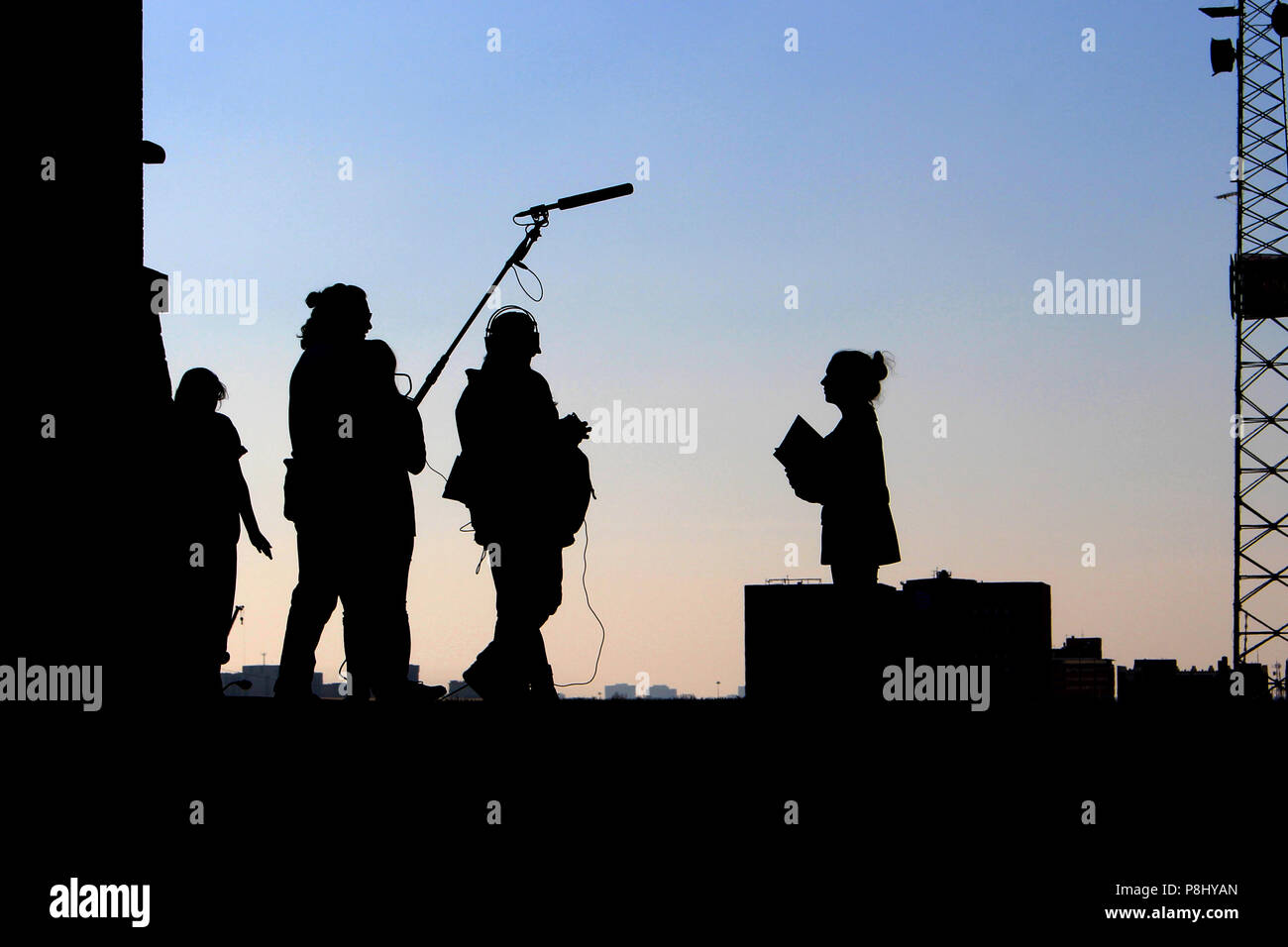 Behind the scenes of a small film crew unit, including audio recordist, boom operator, producers, and talent, silhouetted against the evening sky Stock Photo