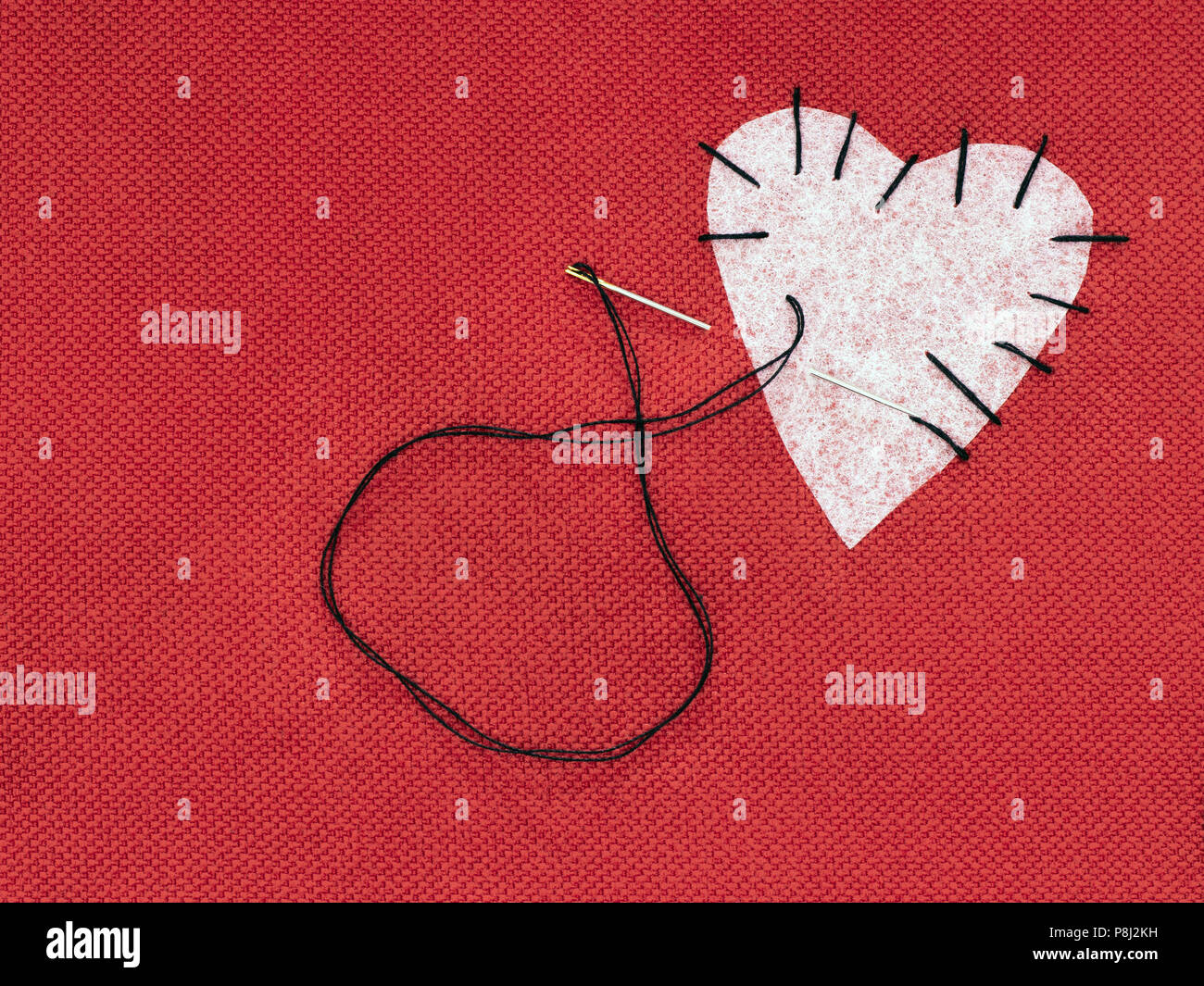 Fabric heart red with white patch and black sewing thread. Mend broken heart concept. Stock Photo