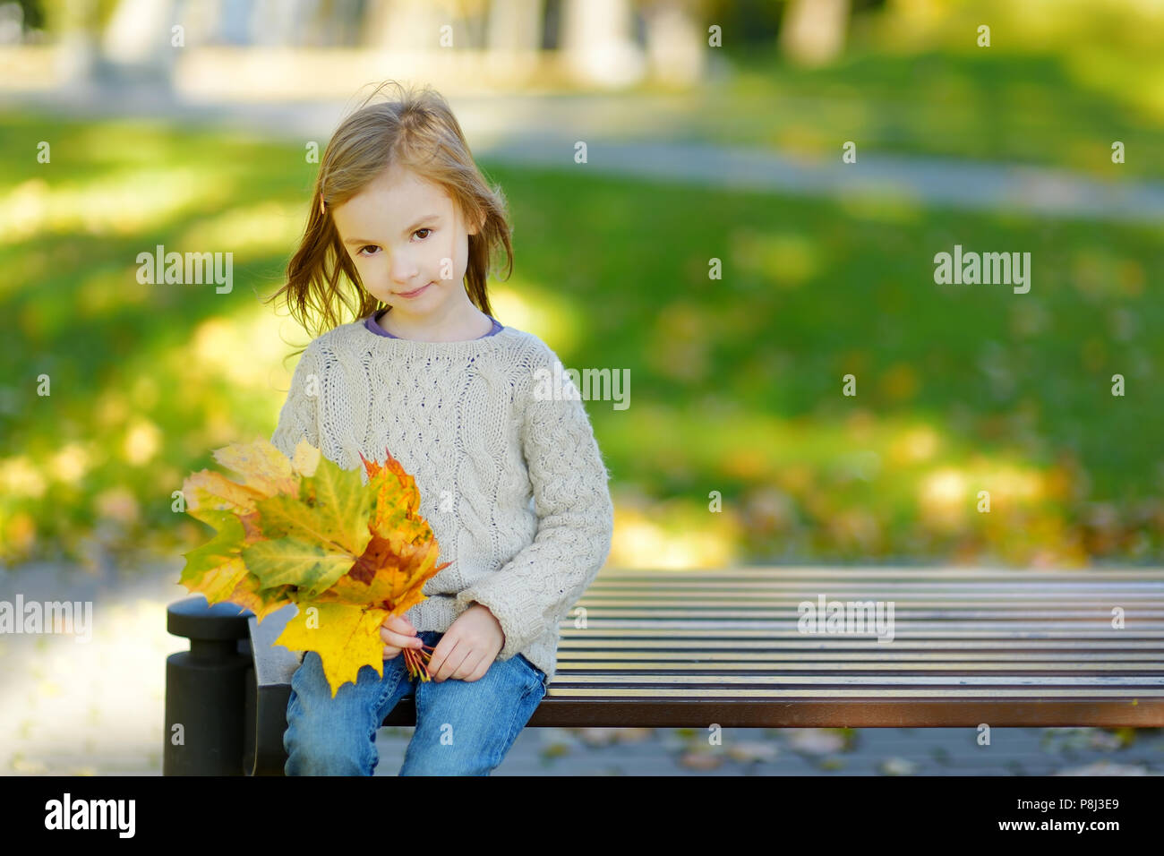 Adorable little girl sitting on a bench in beautiful autumn park on a ...