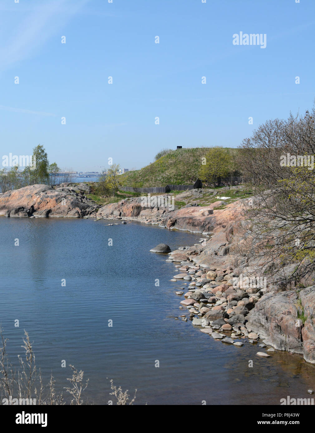 Suomenlinna beach and rocky cove on a sunny day in Finland. Trees and shrubs coming into leaf in spring. Stock Photo