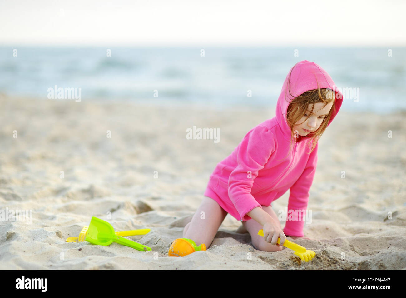 Adorable little girl wearing pink jacket playing on a beach at cold