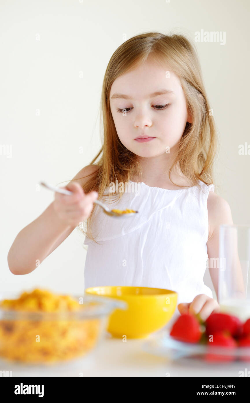Adorable little girl eating cereal with strawberries and drinking milk
