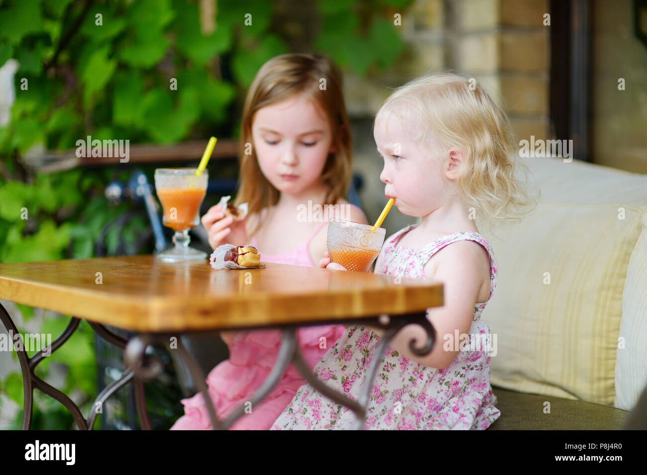 Two little sisters drinking orange juice and eating pastries in an