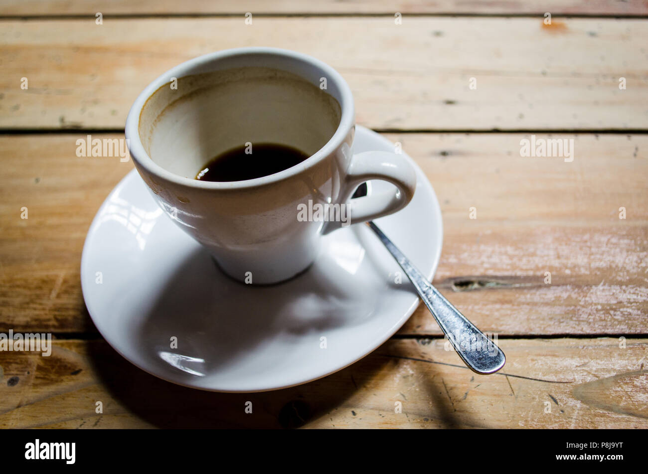 Single white ceramic half full coffee cup and saucer on a rustic wooden table. Stock Photo