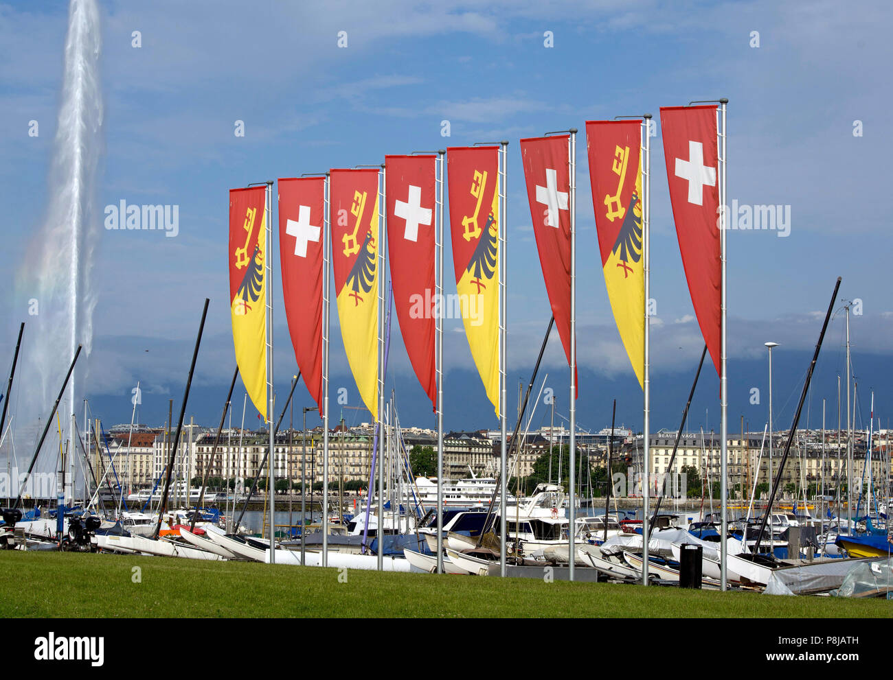 The harbour of Geneva in Switzerland with four Swiss and four Genevan flags in the foreground, the famous Jet d'Eau on the left and dark clouds. Stock Photo