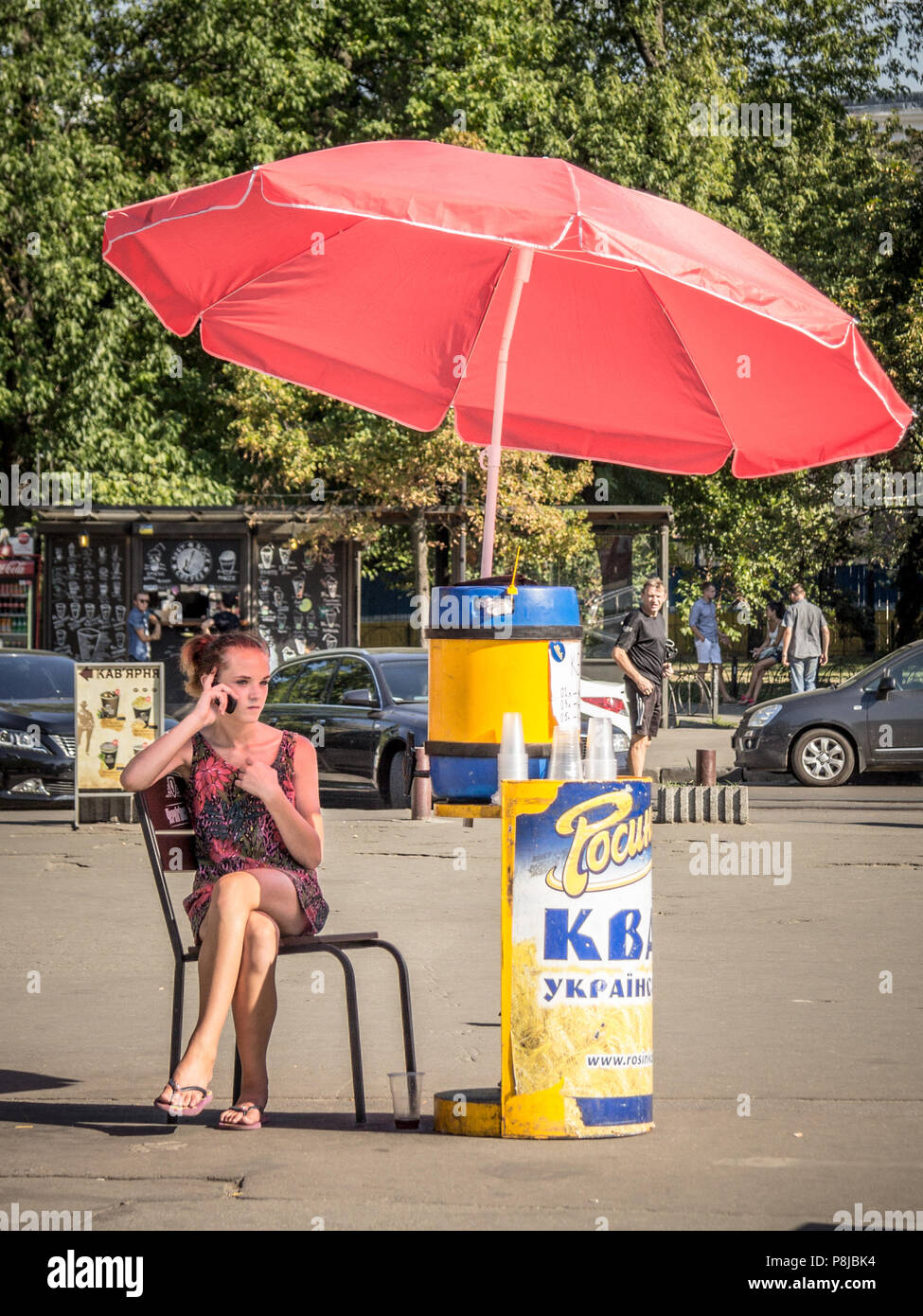 KIEV, UKRAINE - AUGUST 10, 2015: Girl selling Kvass (a popular Eastern European drink) checking her smartphone on a street of the Ukrainian capital ci Stock Photo