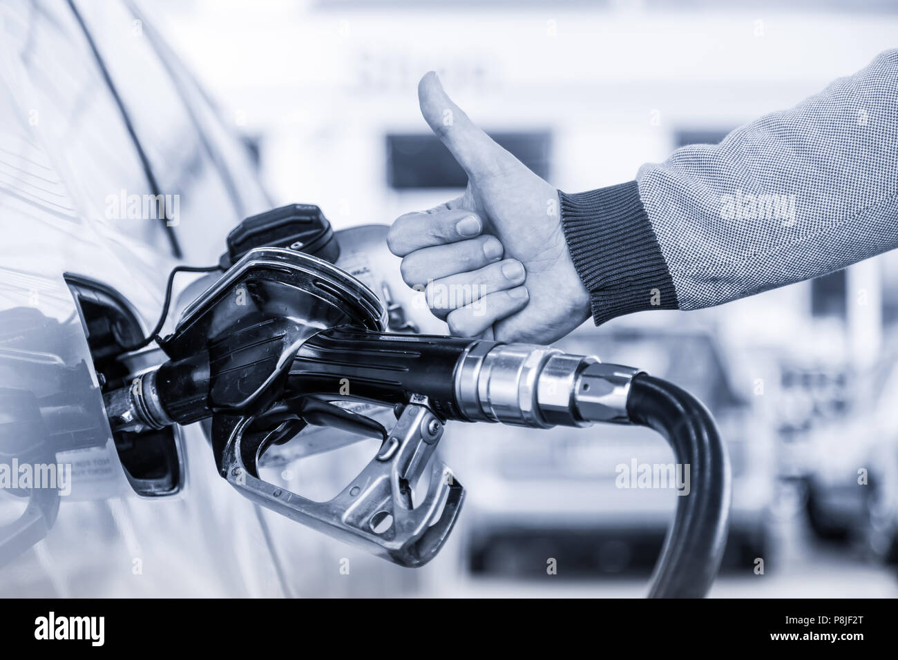 Petrol or gasoline being pumped into a motor vehicle car. Closeup of man, showing thumb up gesture, pumping gasoline fuel in car at gas station. Stock Photo