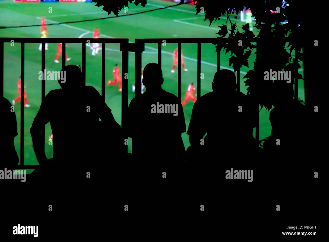Natural silhouettes of  football fans spectators watching soccer match on big screen on city square Stock Photo