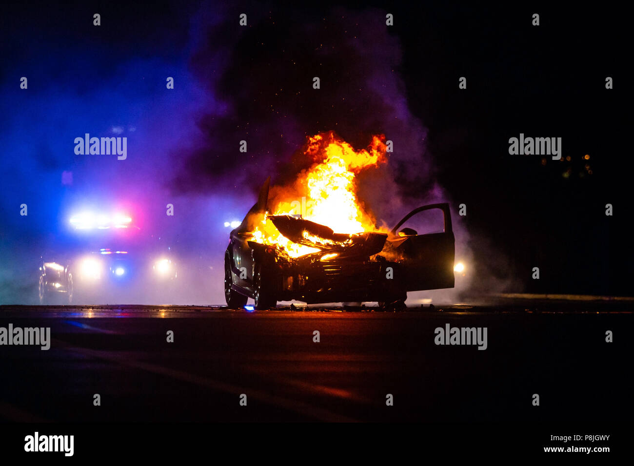 Car on fire at night with police lights in background noone Stock Photo
