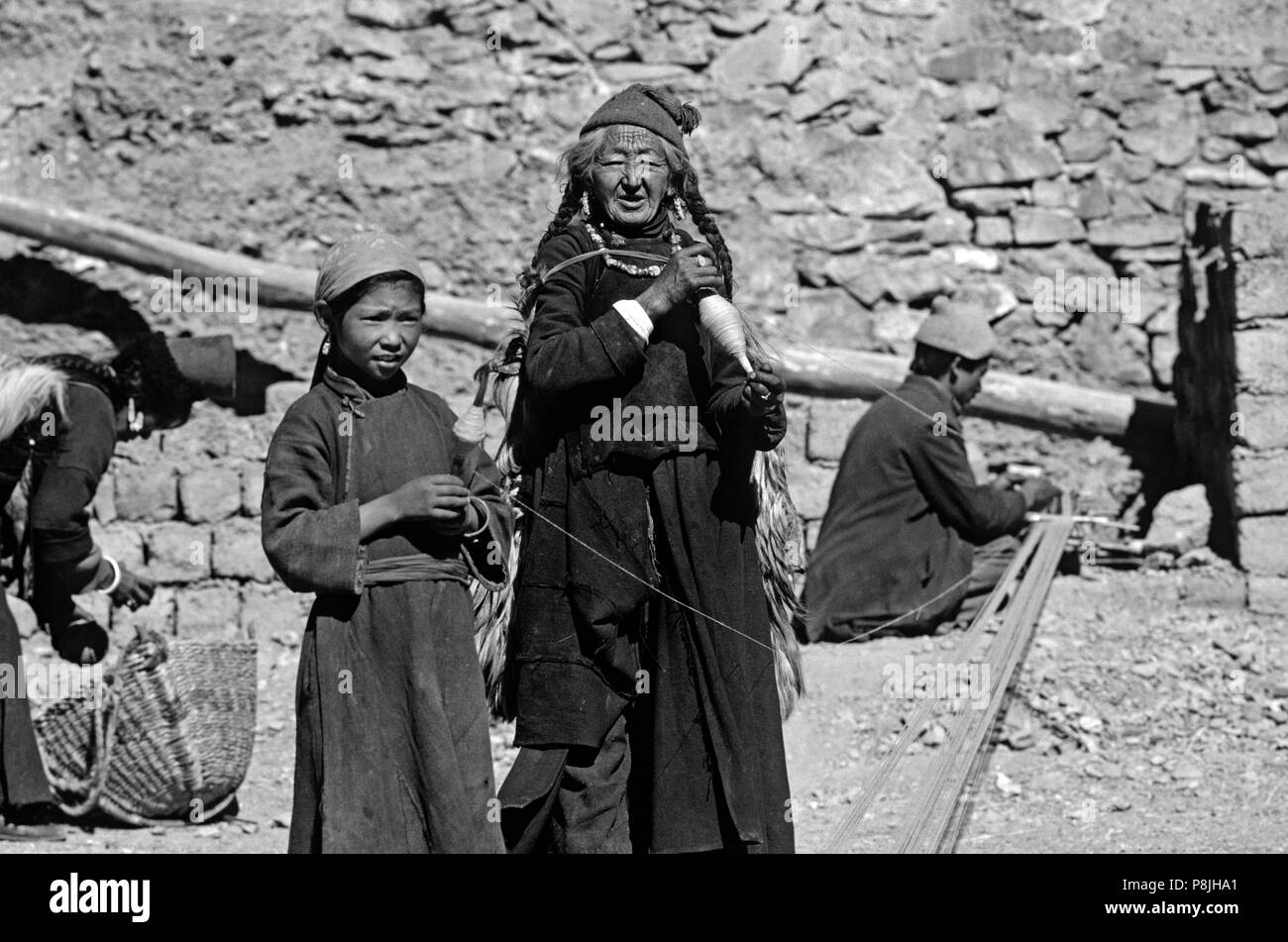 LADAKHI WOMEN wearing HATS and turquoise and coral necklaces preparing a loom to make cloth in LAMAYURU village - LADAKH, INDIA Stock Photo