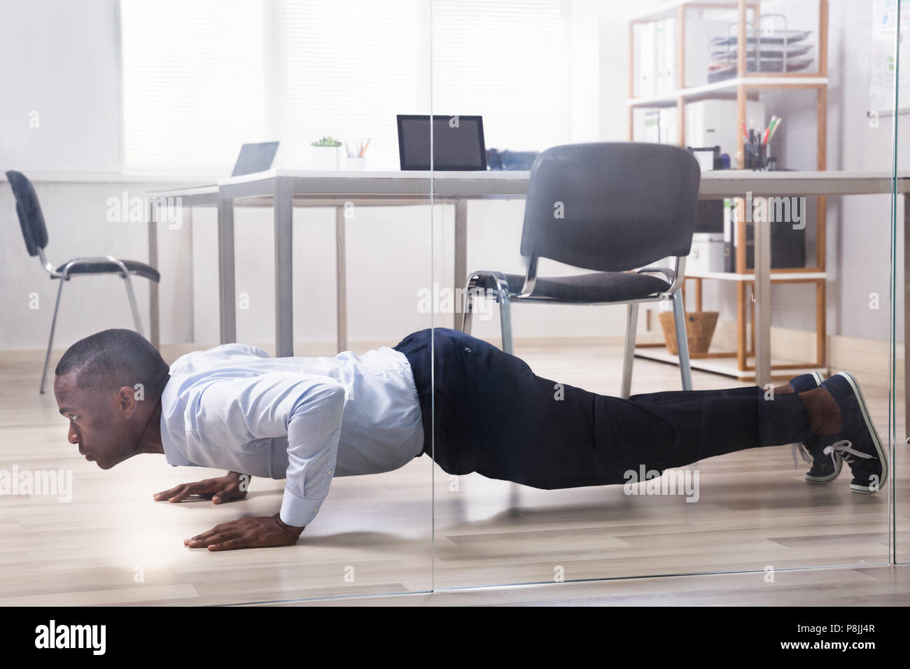 Young African American Man Doing Pushup In Front Of Closed Glass Door Stock Photo