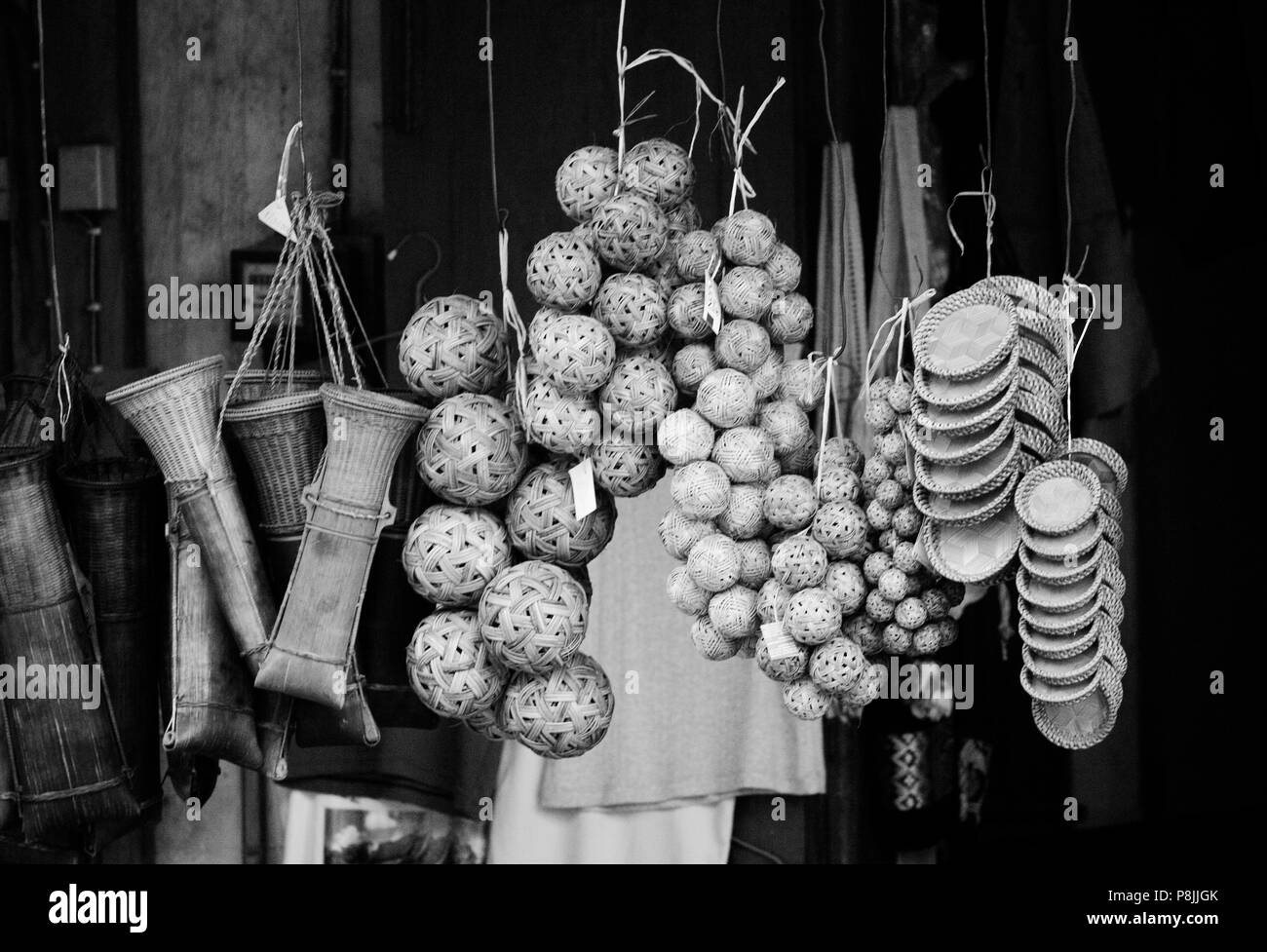 Hand woven rattan baskets, kick balls and machete holders hang in a shop - LUANG PROBANG, LAOS Stock Photo