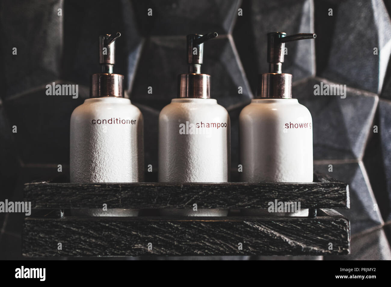 https://c8.alamy.com/comp/P8JMY2/three-white-metal-bottles-of-shampoo-conditioner-shower-gel-on-wooden-shelf-in-modern-hotel-bathroom-with-textured-black-wall-P8JMY2.jpg