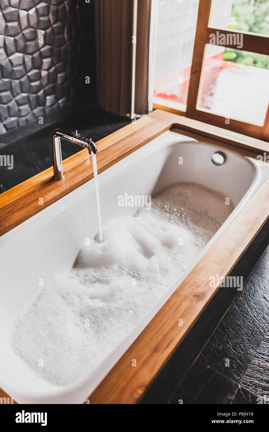 Water filling bath with foam. Modern style of bathroom with wooden edge