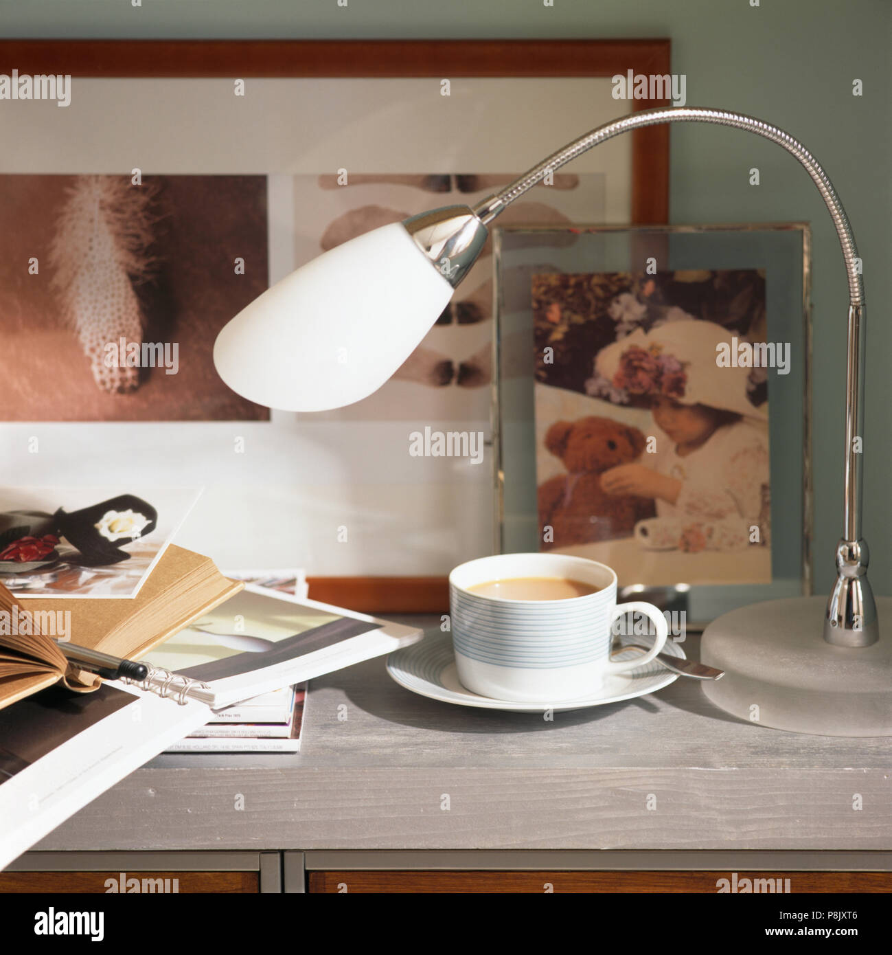 Close-up of a chrome lamp on table with a cup of coffee and a pile of notebooks Stock Photo