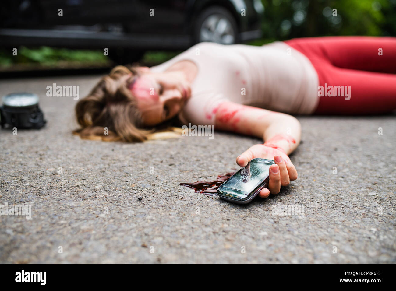 Young injured woman with smartphone lying on the road after a car accident, unconscious. Stock Photo