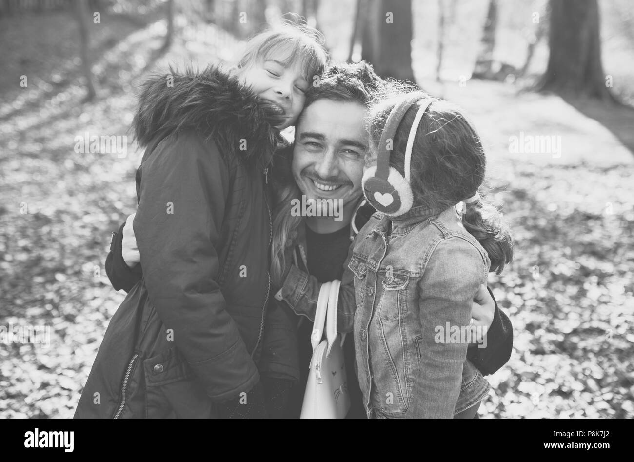 Dad and father on a family walk with his two daughters, hugging in the woods and laughing together. A black and white image. Stock Photo