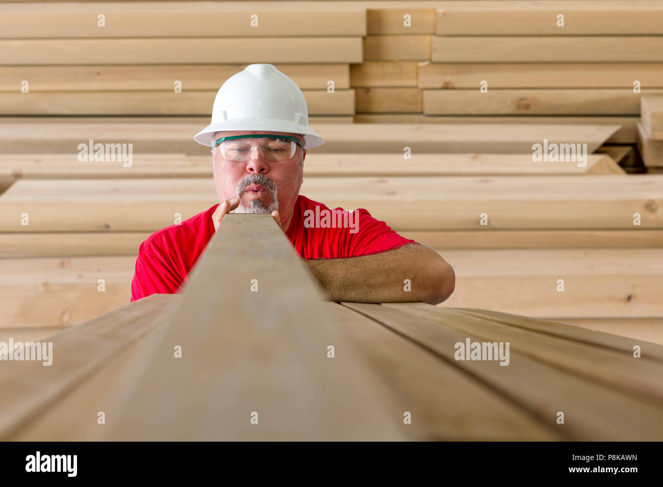 Man with helmet and protective eyewear taking wooden construction plank Stock Photo