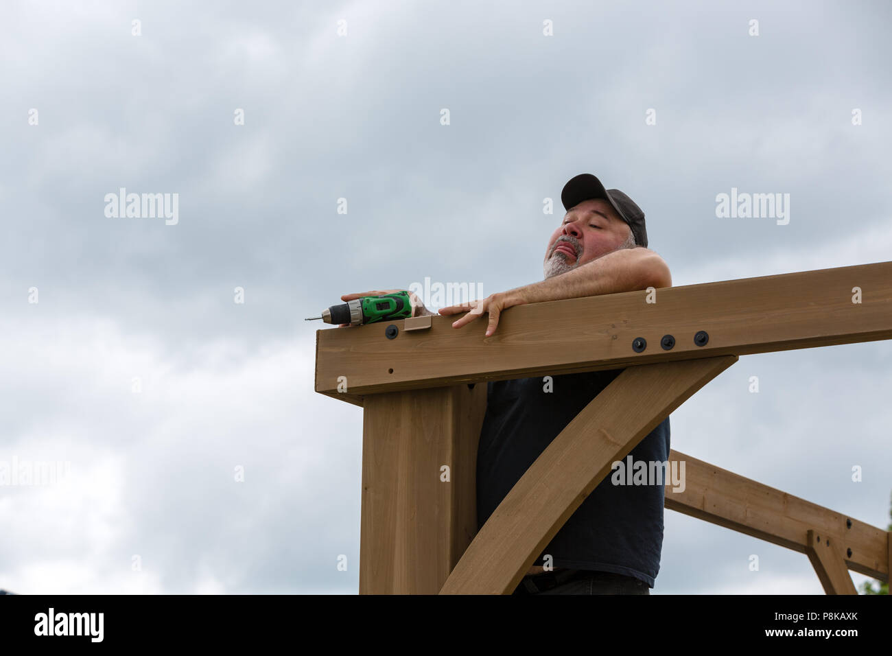 Mature man falling while assembling wooden pergola with cordless drill-driver Stock Photo