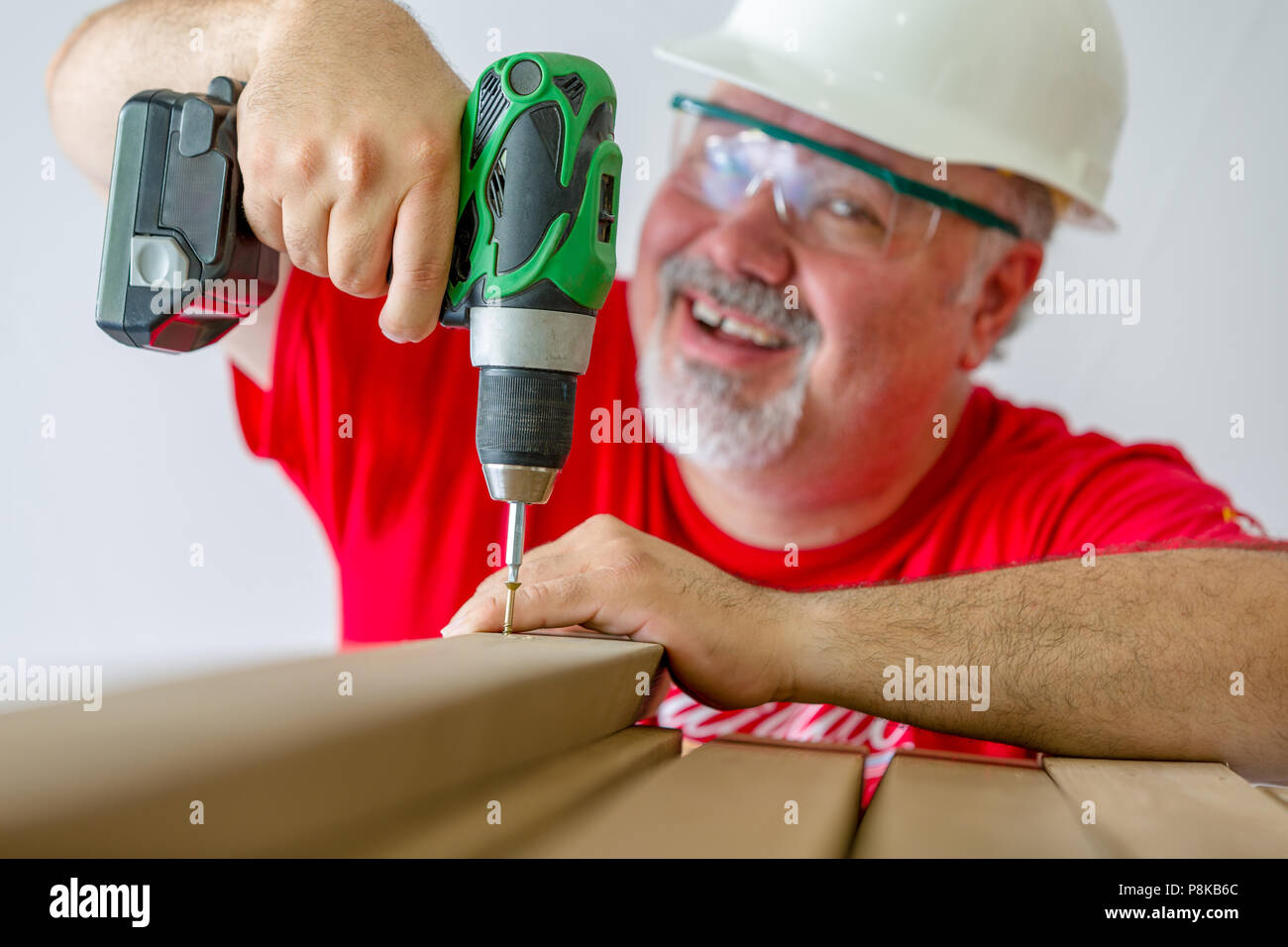 Portrait of smiling man using drill-drive while building wooden construction Stock Photo
