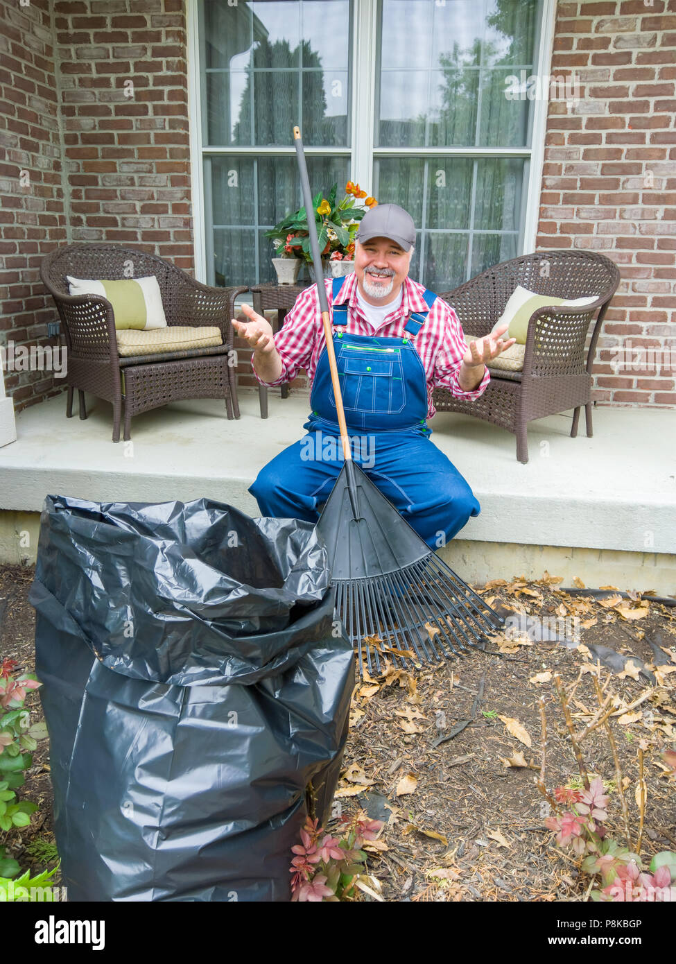 Happy gardener finished with raking the leaves in his garden sitting on his porch gesturing with his hands grinning at the camera Stock Photo