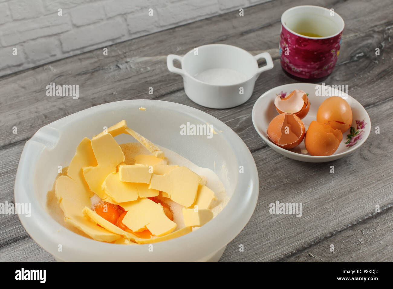 Cake preparation - plastic bowl with flour and yolk, egg shells and salt in background on gray wood table. Stock Photo