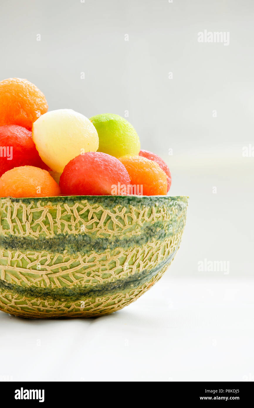Four different kinds of melon made into ball place in the skin of a century-melon creating a colourful vertical image with a light background to ad co Stock Photo