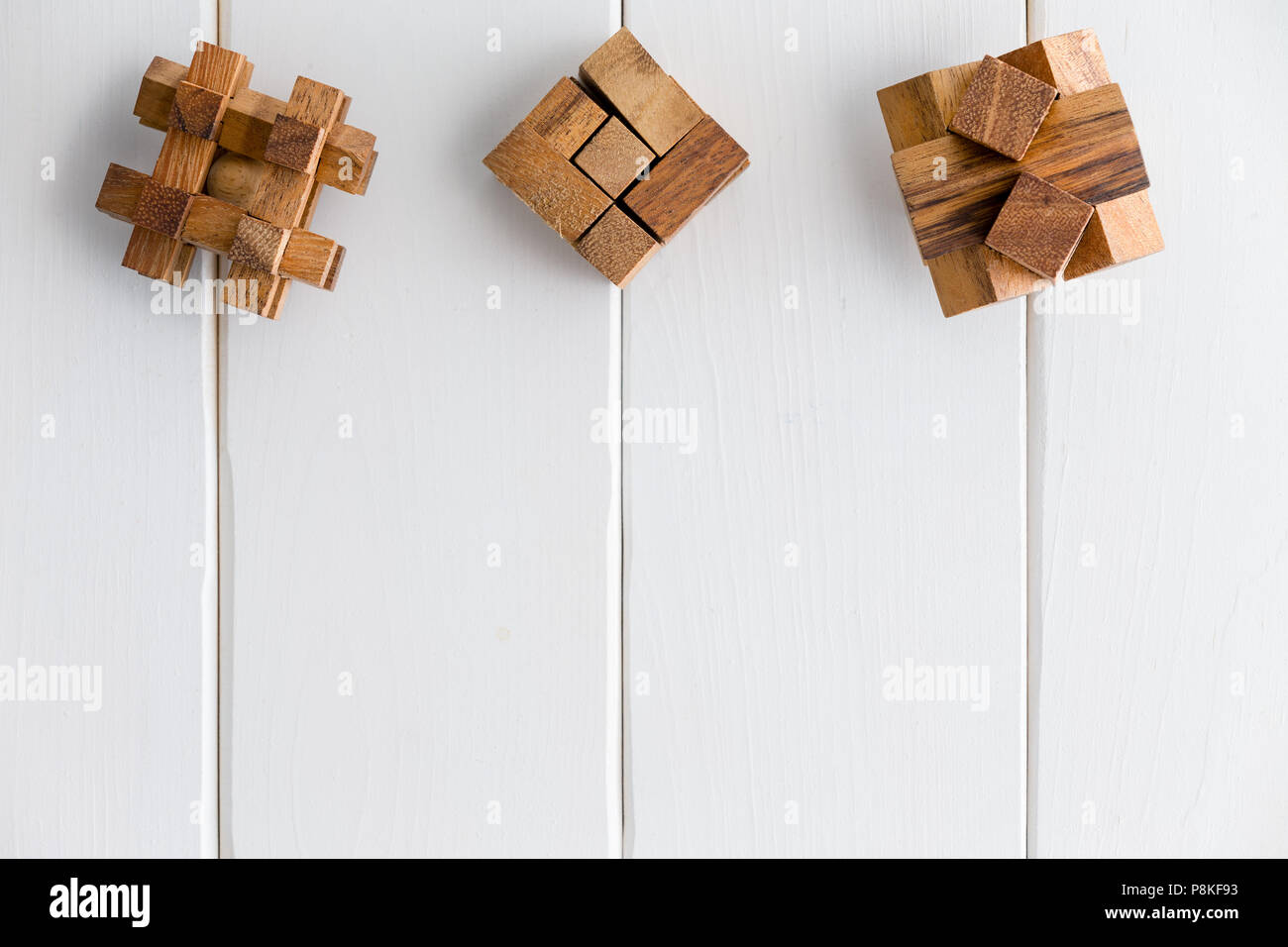 Three geometric interlocked wooden puzzles arranged in a neat line as a top border on white painted wood boards with copy space Stock Photo