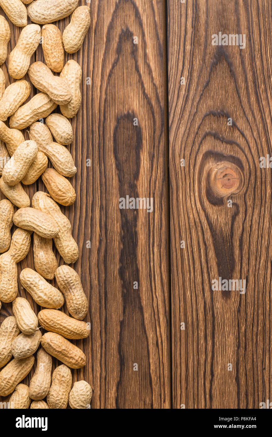Vertical side border of whole healthy nutritious peanuts in their shells or pods on wood with a woodgrain texture and copy space Stock Photo
