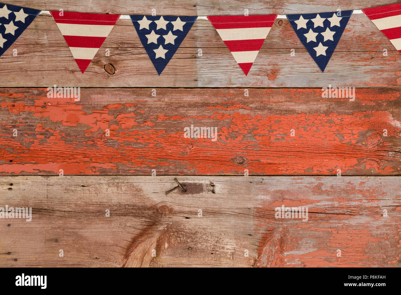 Patriotic bunting with the stars and stripes of America in triangular flags on a string over rustic weathered wood with peeling red paint and copy spa Stock Photo
