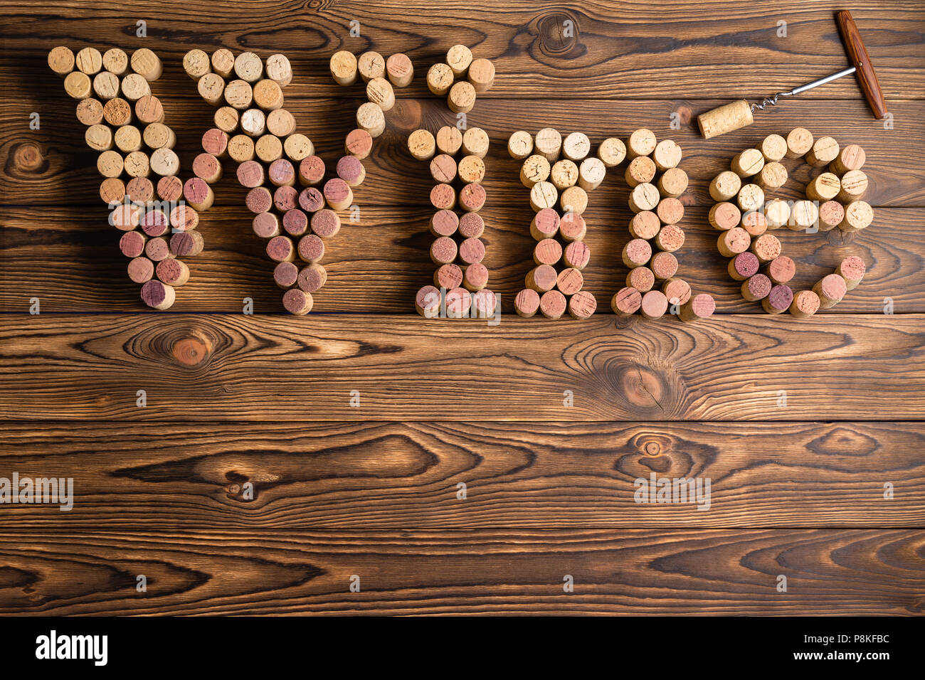 Word Wine formed of used red and white wine bottle corks in graduated colors on a rustic wooden background with an opener or corkscrew and copy space Stock Photo