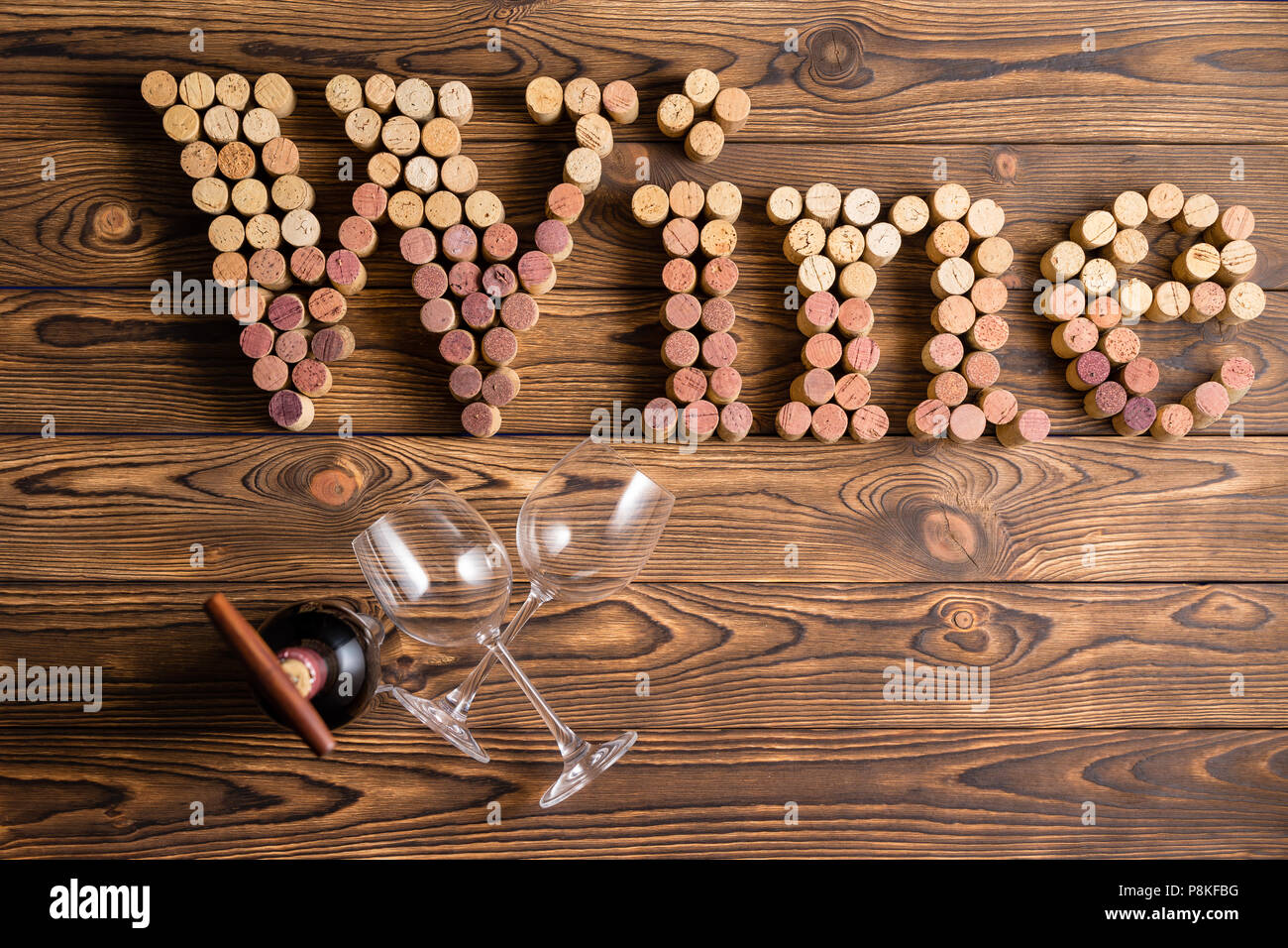 Corks arranged in wine lettering with two glasses and bottle against wooden background Stock Photo
