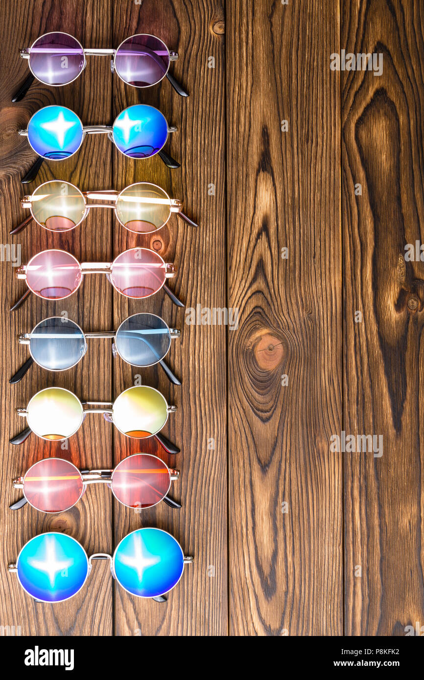 Side vertical border of colorful generic sunglasses with multicolored round lenses and a reflected sun burst on a decorative wood background with copy Stock Photo
