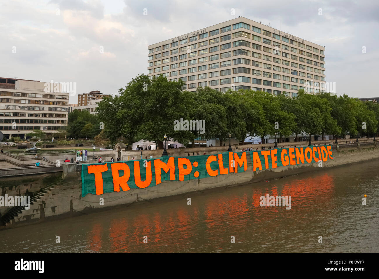 Westminster, London, 12th July 2018. Campaigners against climate change protest over Donald Trump's visit by dropping a giant banner reading 'Trump: Climate Genocide' at St Thomas’ Hospital Gardens, opposite the Houses of Parliament in Westminster. The huge banner, 100 metres x 9 metres large, is to raise awareness about the US president's climate policies. Credit: Imageplotter News and Sports/Alamy Live News Stock Photo