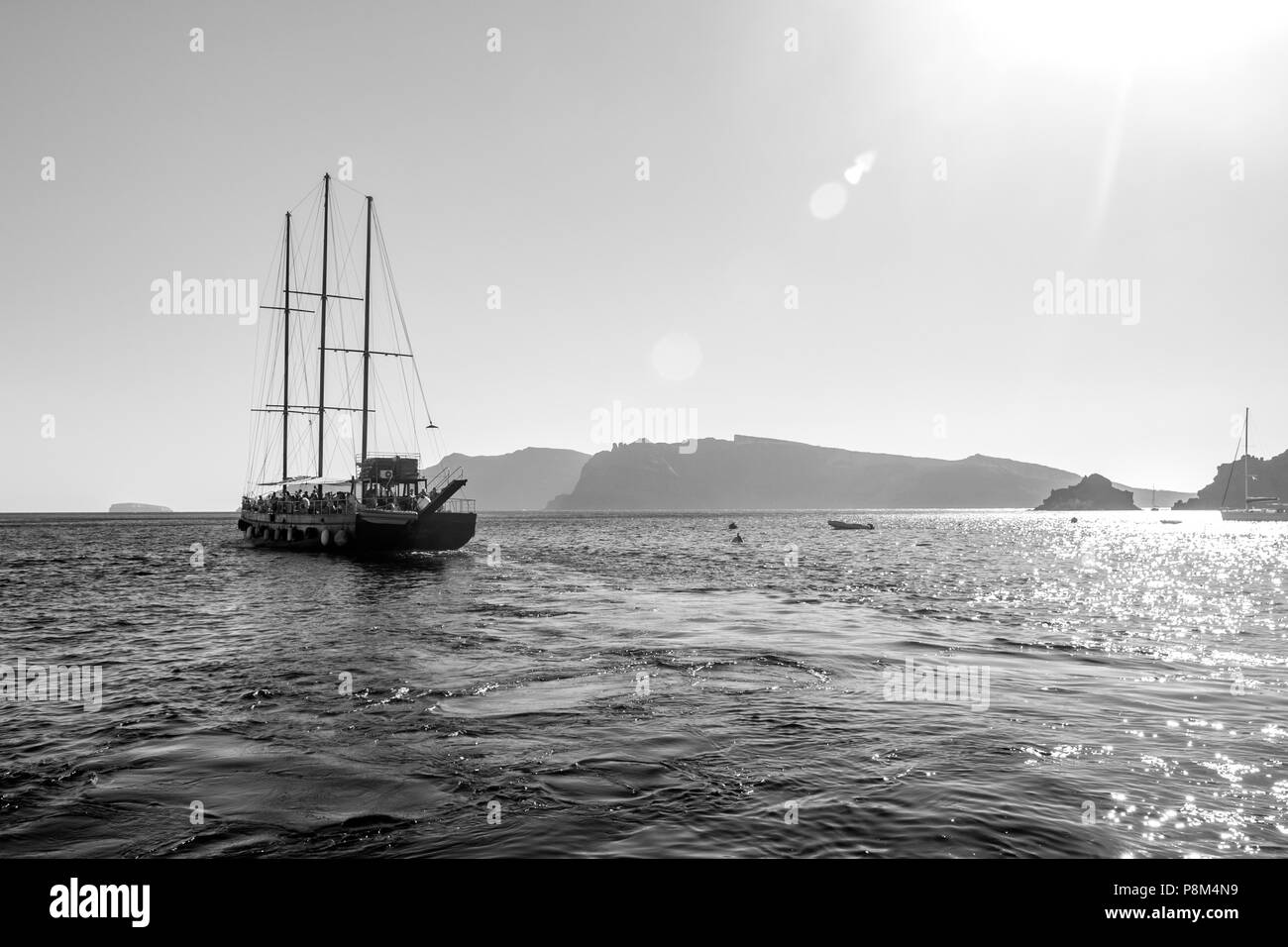 Tourist boat sailing away in Santorini, Greece. Amazing daytime view towards the Sun and deep