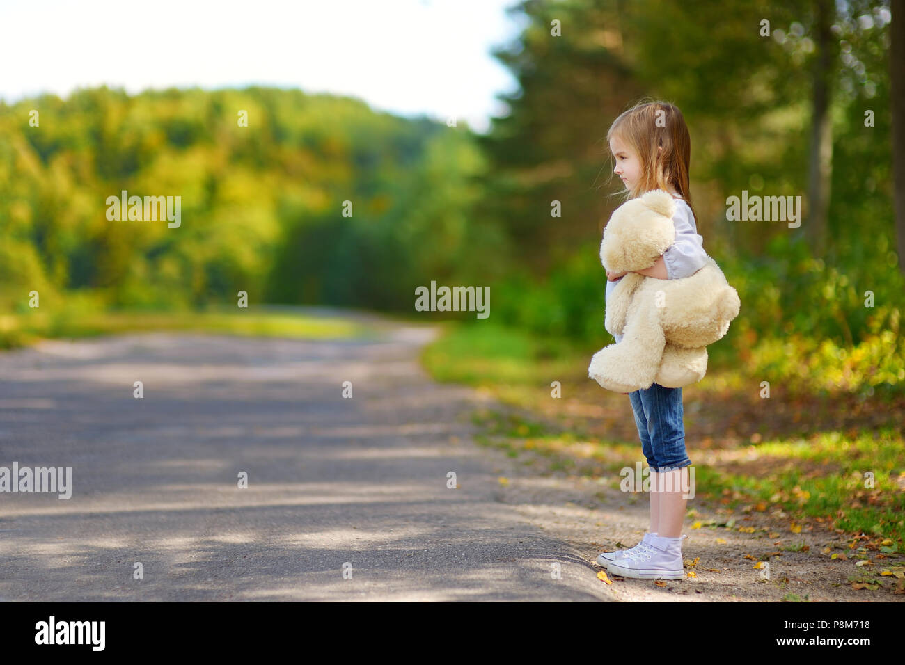 Adorable little girl with a teddy bear standing by the road Stock Photo ...