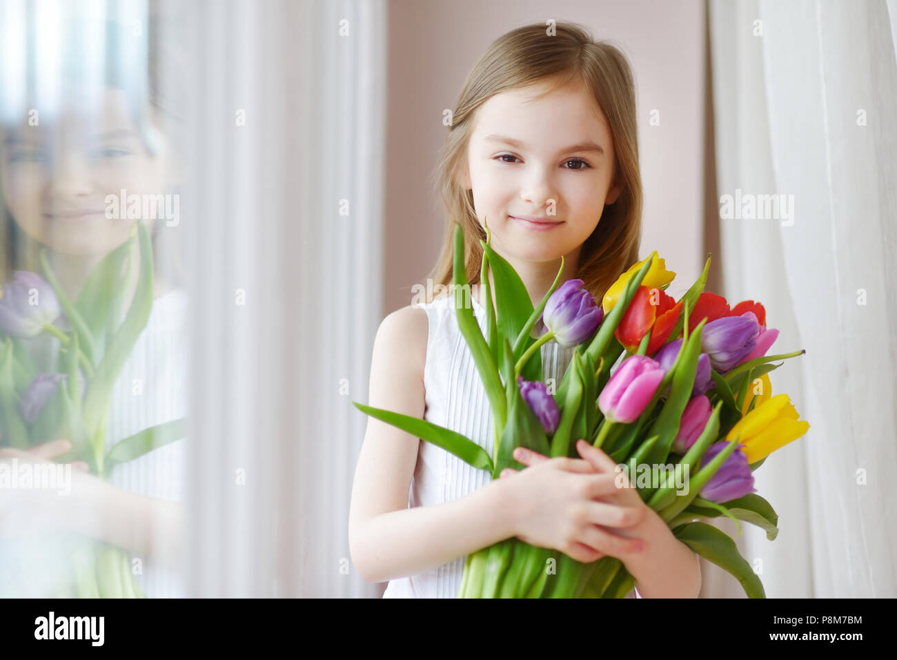 Adorable smiling little girl holding tulips by the window Stock Photo