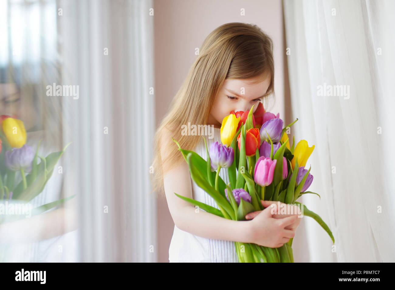 Adorable smiling little girl holding tulips by the window Stock Photo