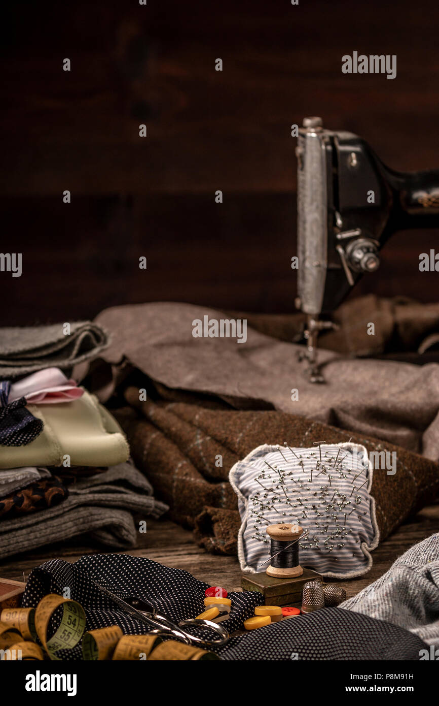 Beautiful pieces of fabric, sewing spools, scissors, tape measure and glasses set beautifully on rough wooden plank table Stock Photo