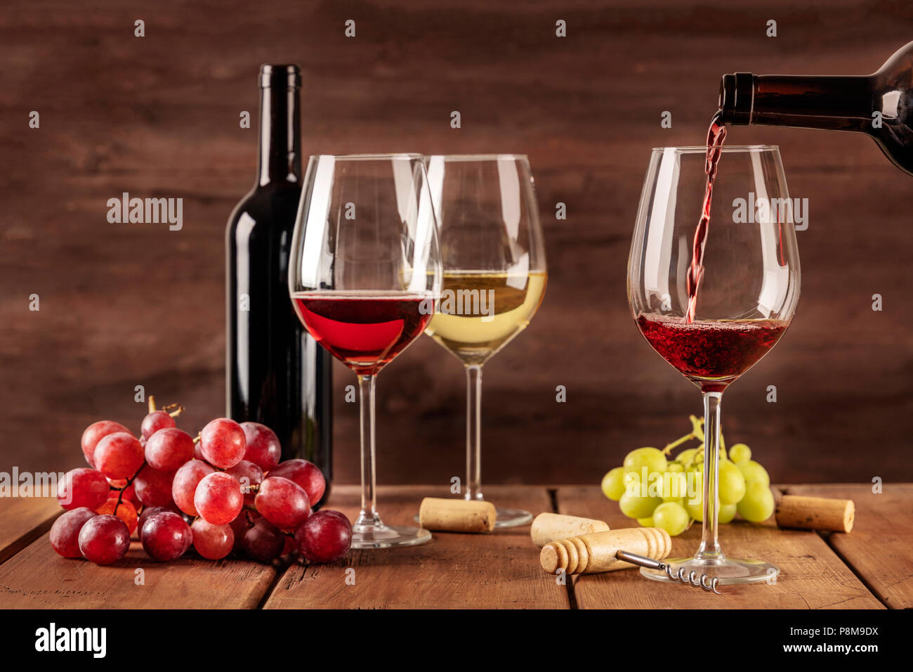 Red wine being poured into a glass from a bottle, on a dark background,  with copy space and other glasses and grapes in the blurred background.  Design Stock Photo - Alamy