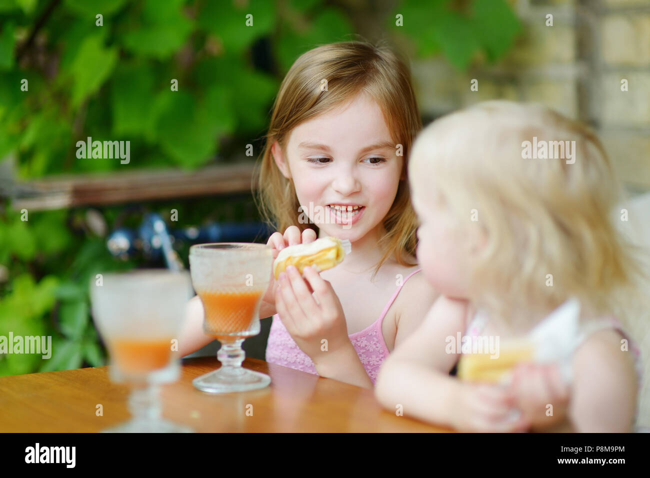 Two little sisters drinking orange juice and eating pastries in an